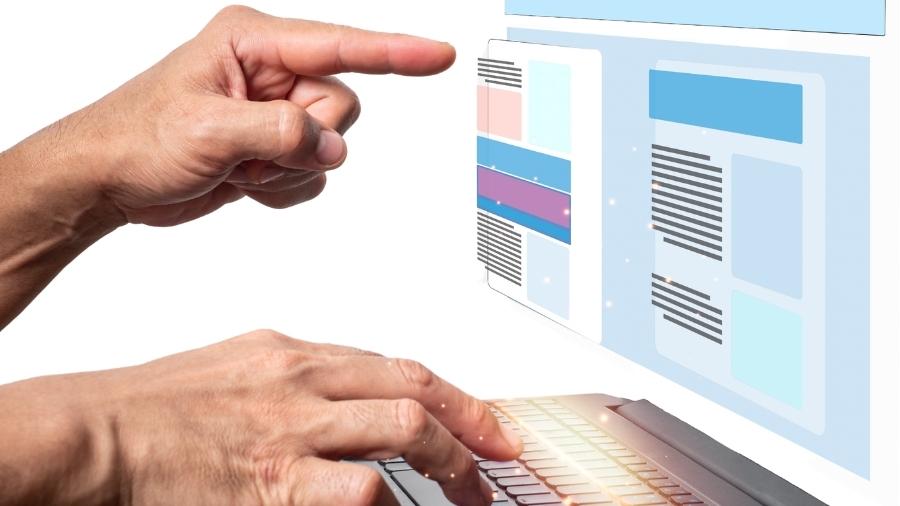 Foto de una mano sobre un teclado y otra tocando una pantalla de ordenador, de forma simulada.